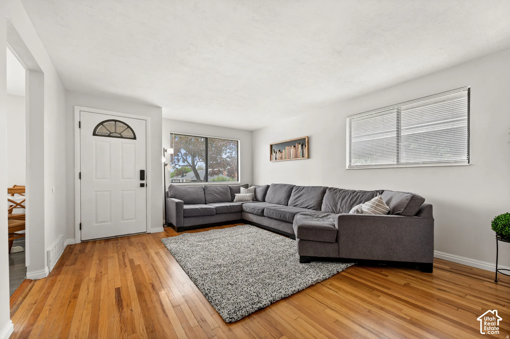Wood-finish flooring throughout, white paneled entry door with an arched glass insert, and a large front-facing window