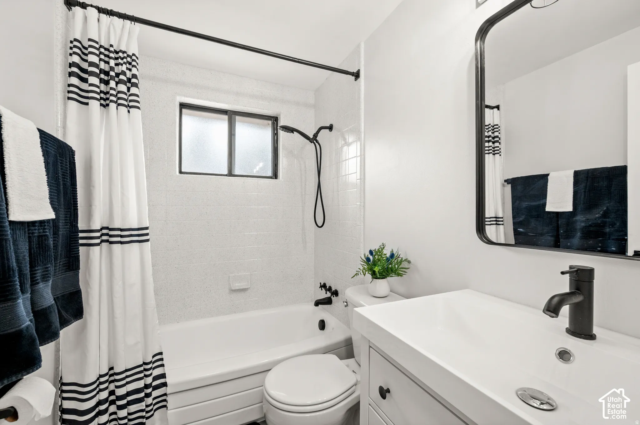 Bathroom featuring a white vanity with integrated sink, black framed mirror, and a tub with white subway tile surround and a window