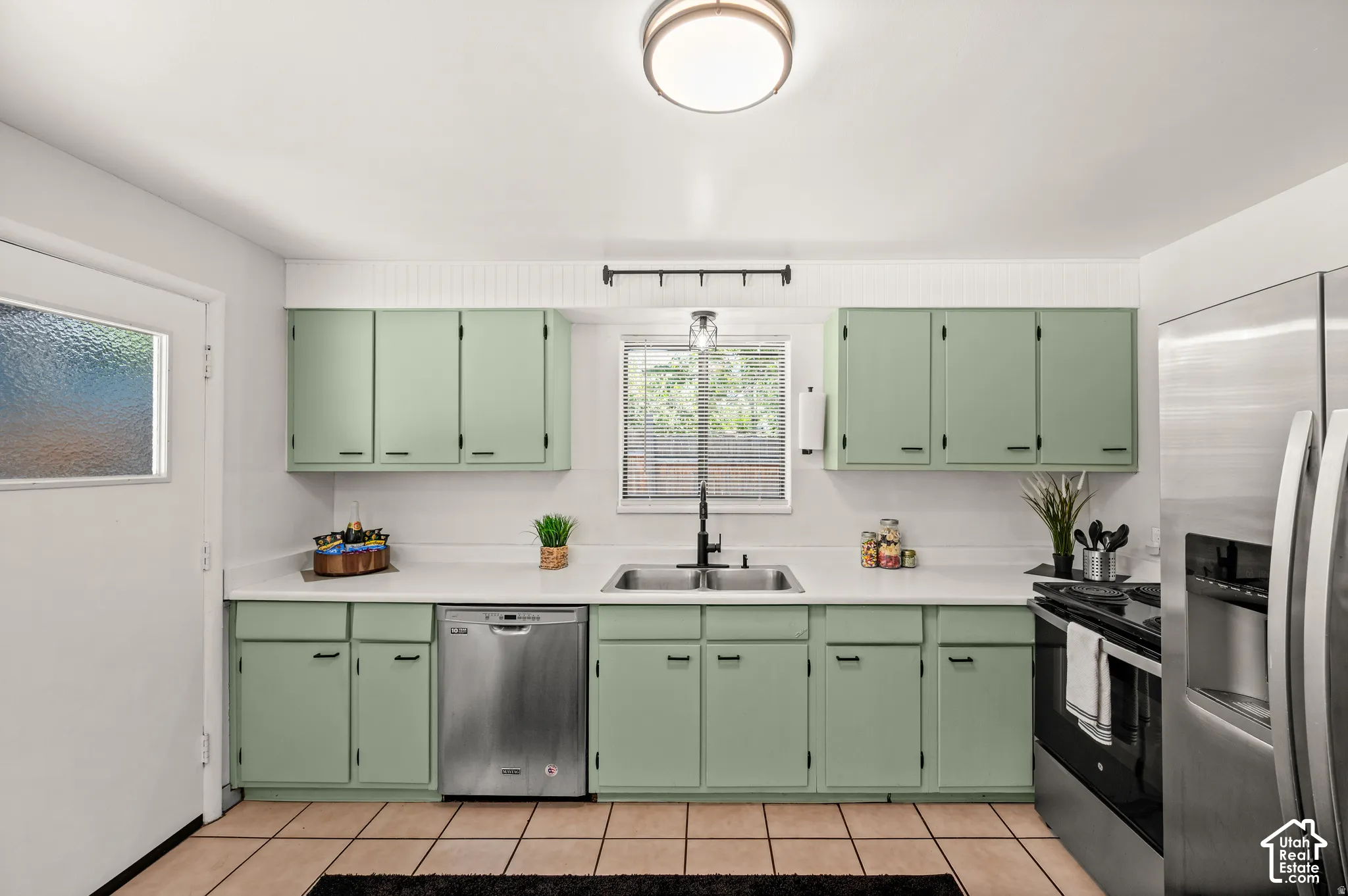 Kitchen featuring green cabinetry, light-colored countertops, stainless steel appliances, and tile flooring