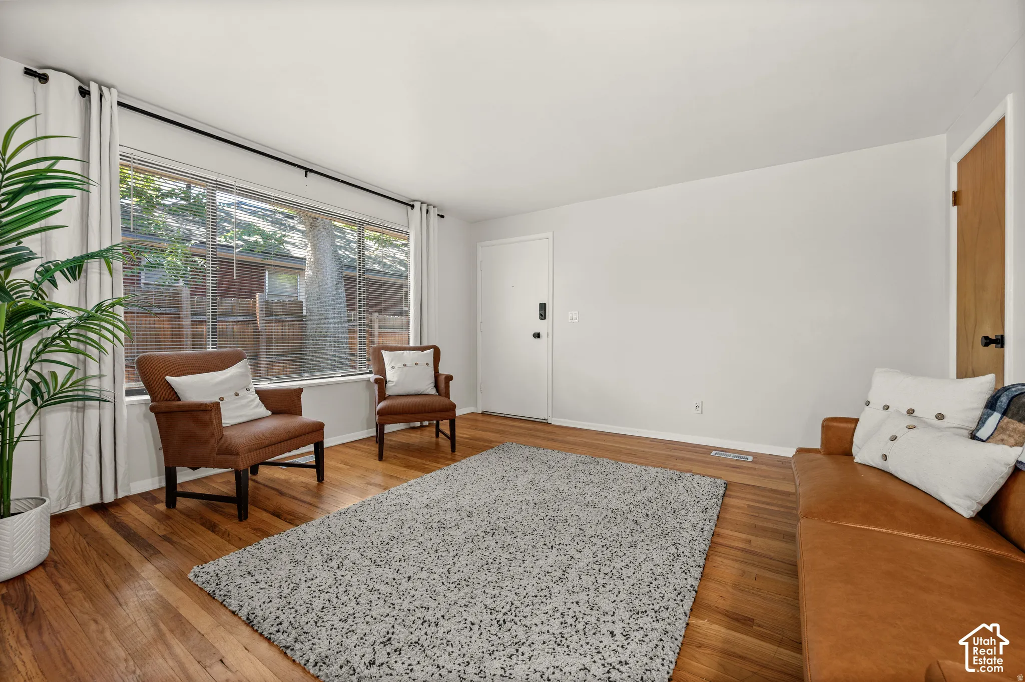 Hardwood flooring throughout, large picture window, white walls, and a white entry door with matte black hardware