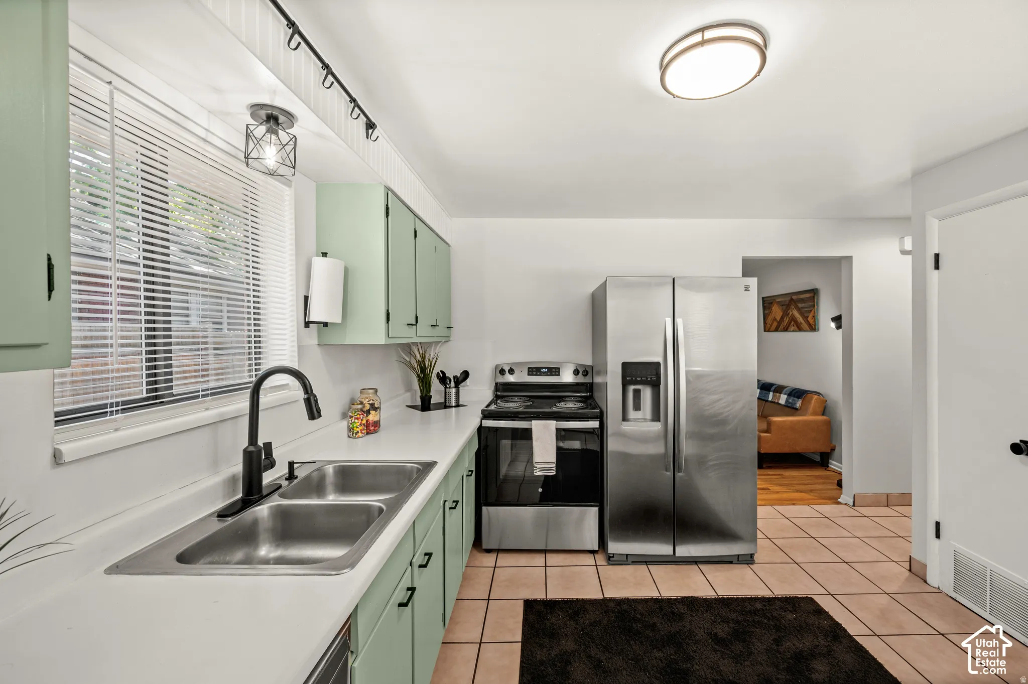 Kitchen featuring white countertops, light green cabinetry, a stainless steel double basin sink with a matte black faucet, and tiled flooring