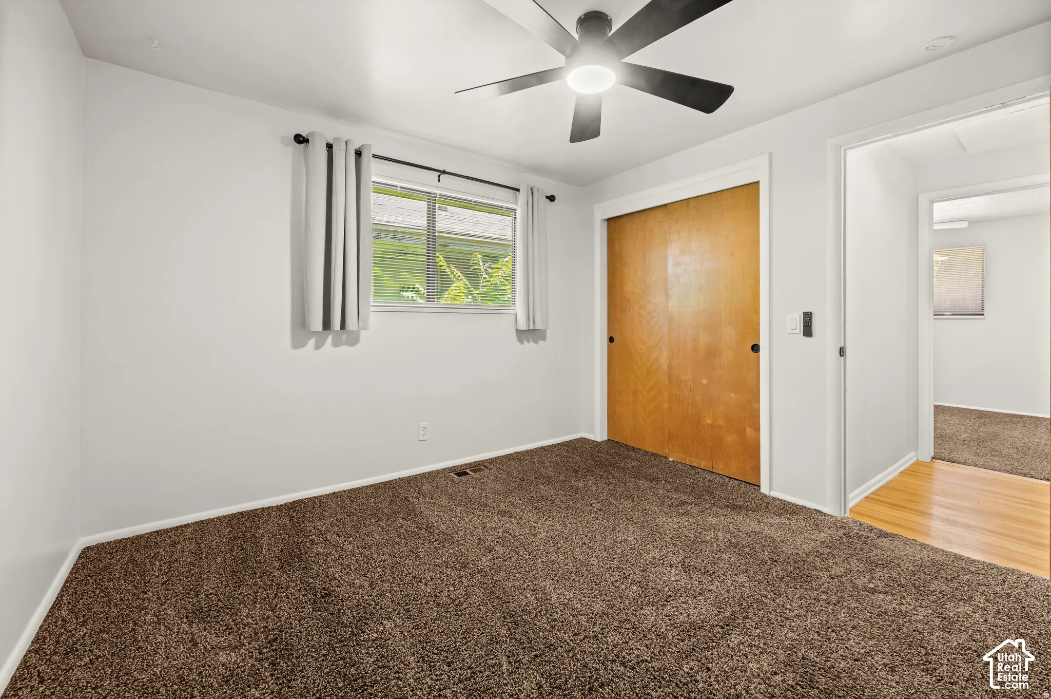 Neutral wall color, brown carpet flooring, ceiling fan, wood closet doors, and hardwood flooring in the doorway