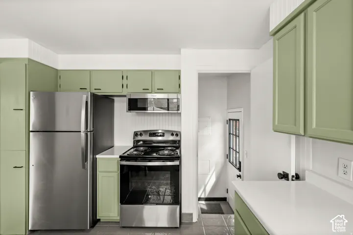 Stainless steel appliances, white countertops, green cabinetry, beadboard wall paneling, and tile flooring