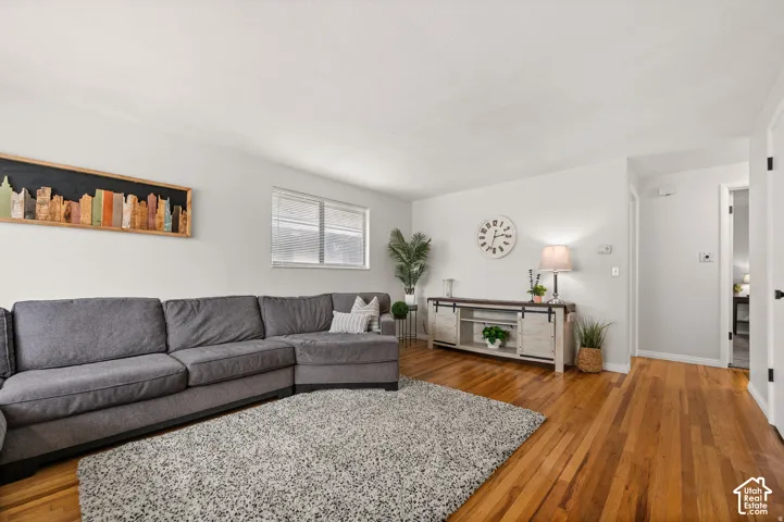 Hardwood flooring, painted white walls, recessed window with blinds, white trim, and a white interior door with matte black hardware