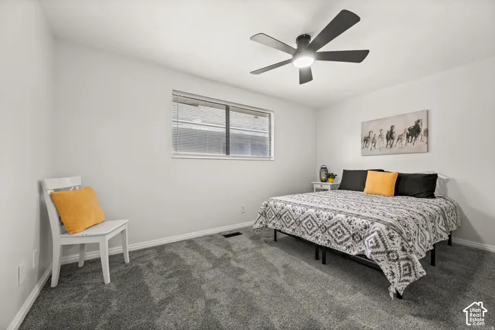 Gray carpet flooring with a window featuring blinds, a ceiling fan with integrated lighting, and white wall finishes