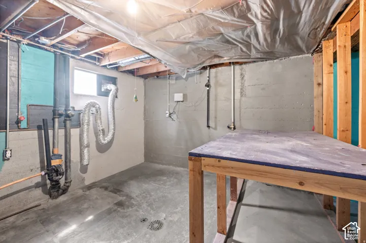 Concrete floor, exposed ceiling joists, utility piping, small window, built-in workbench