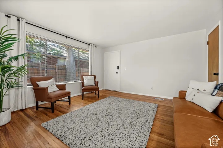 Hardwood flooring throughout, large picture window, white walls, and a white entry door with matte black hardware
