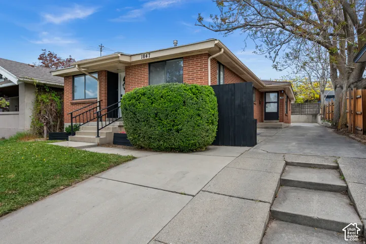 Red brick exterior with white trim, concrete driveway, front entry with black railing, and mature landscaping