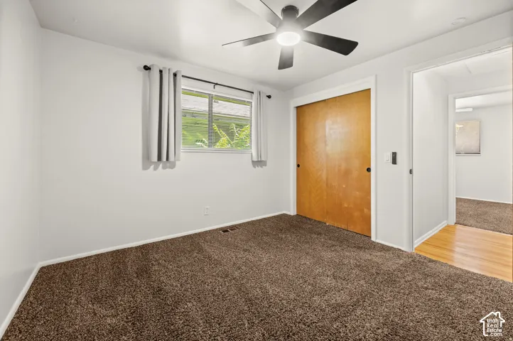 Neutral wall color, brown carpet flooring, ceiling fan, wood closet doors, and hardwood flooring in the doorway