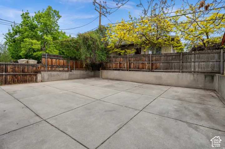 Paved concrete outdoor area with perimeter wood fencing and concrete retaining walls