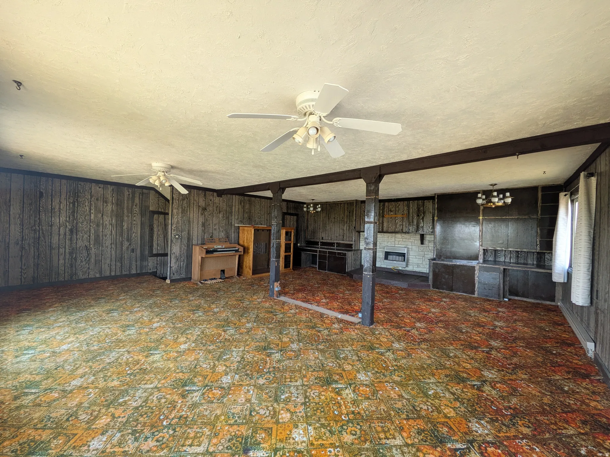 Spacious interior featuring wood-paneled walls, exposed support beams, built-in cabinetry, and ceiling fans
