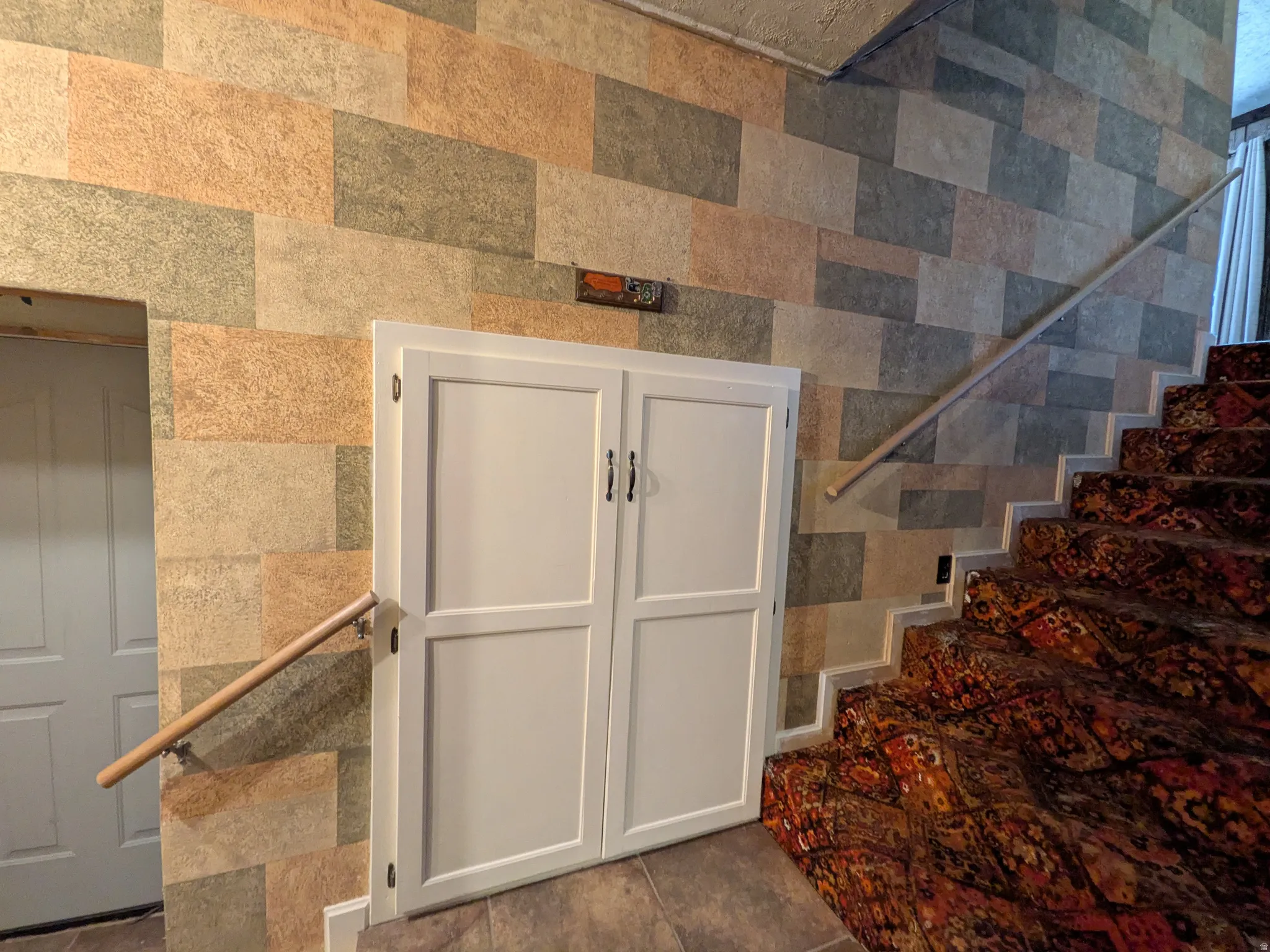 Textured wall covering, white paneled doors, hardwood handrails, and patterned stair runner