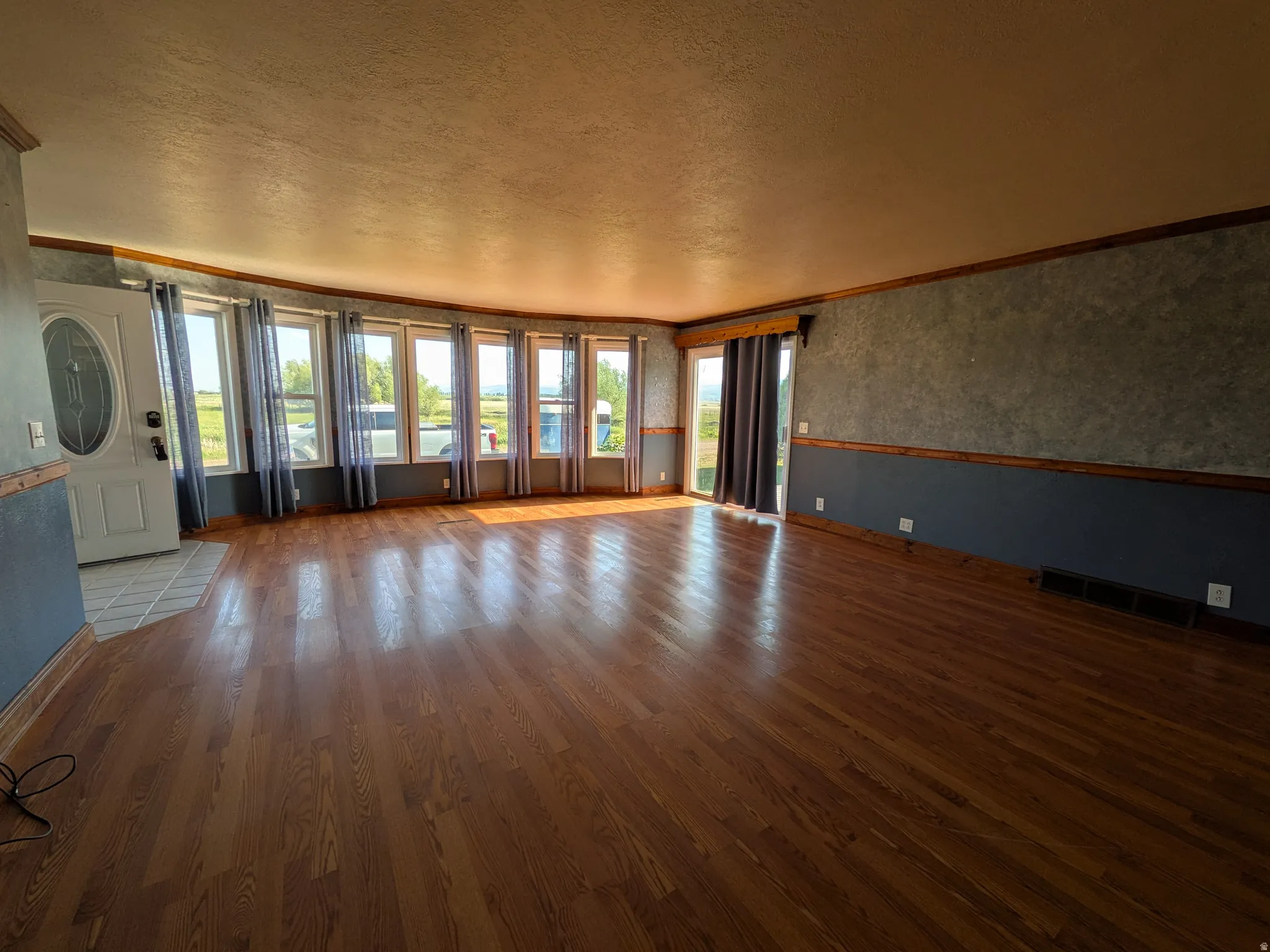 Hardwood flooring, multiple windows, a sliding glass door, and a white entry door with an oval-shaped glass insert