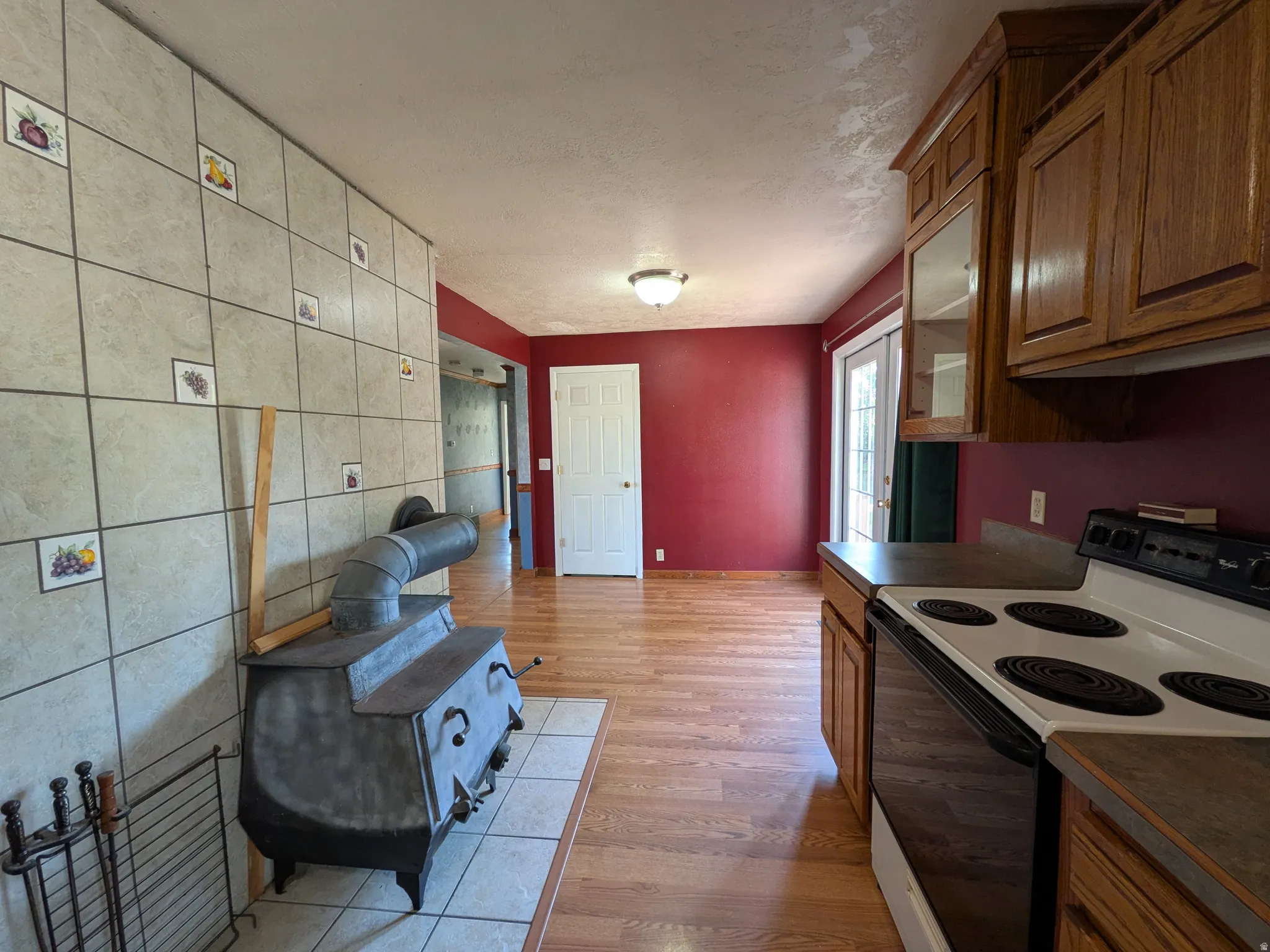Wood-finish flooring, built-in cabinetry, ceramic tile wall, wood-burning stove, and a ceiling-mounted light fixture