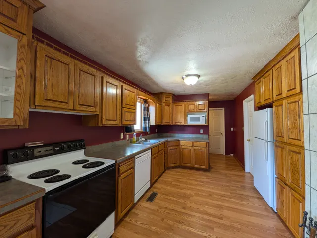 Kitchen with wood-finish flooring, wood cabinetry, and a complete suite of white appliances