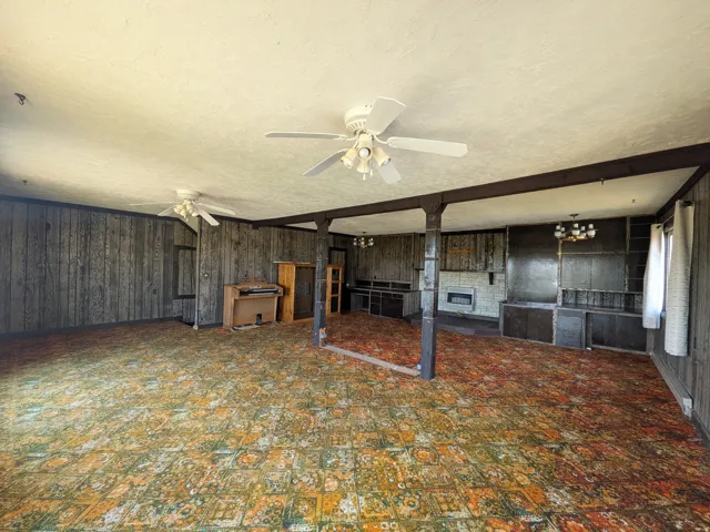 Spacious interior featuring wood-paneled walls, exposed support beams, built-in cabinetry, and ceiling fans