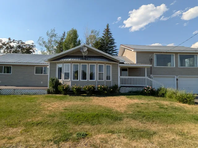 Multi-level exterior with metal roofing, an enclosed bay window sunroom, a covered front porch with white railing, and an attached two-car garage