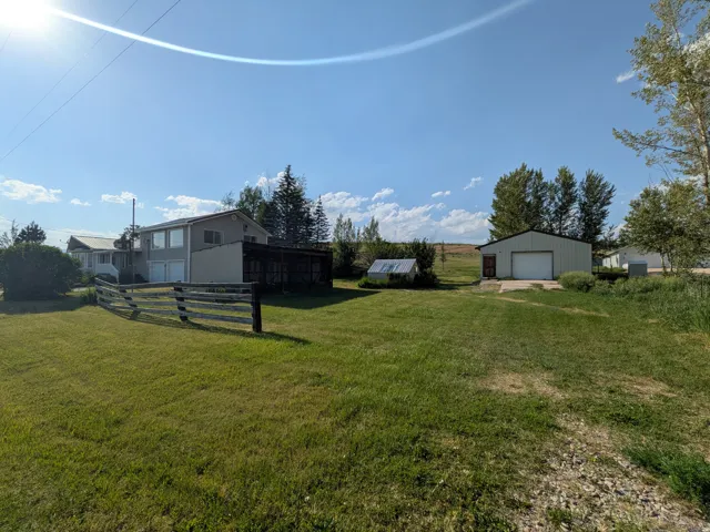 Expansive lot featuring a two-story residence with attached garage, detached metal workshop with roll-up door, and split-rail fencing