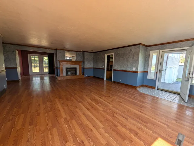 Expansive room featuring wood-finish flooring, a fireplace with a wood mantle, and double French doors opening to an exterior space