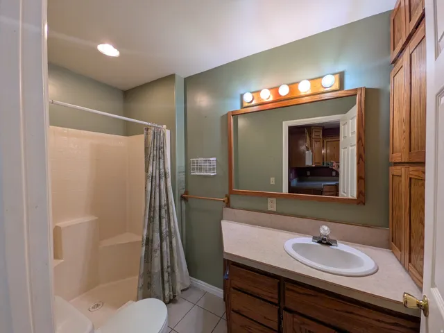 Vanity with integrated sink and countertop, wood-finish cabinetry, full-width mirror with overhead lighting, and a shower-tub combination