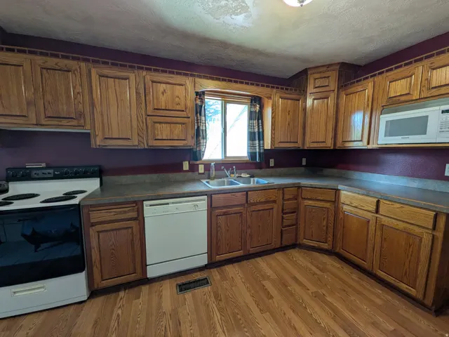 Wood-finish flooring with extensive wood cabinetry, L-shaped countertop, double basin sink, and built-in microwave