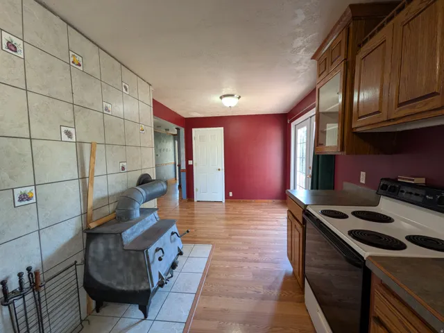 Wood-finish flooring, built-in cabinetry, ceramic tile wall, wood-burning stove, and a ceiling-mounted light fixture