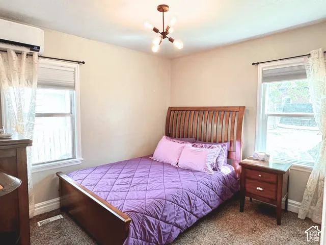 Recessed lighting fixture, two windows with window treatments, wall-mounted air conditioning unit, and textured carpeting