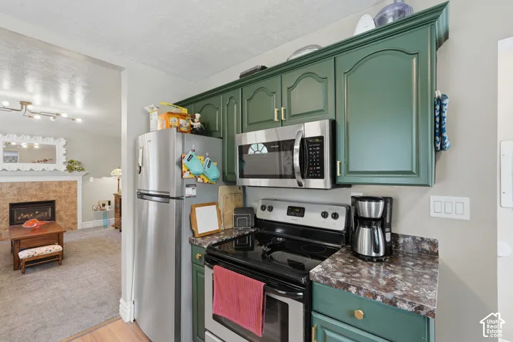Green painted cabinetry with gold-tone hardware, stainless steel appliances, and dark speckled countertops