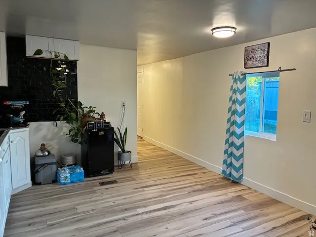 Wood-finish flooring, white cabinetry, black subway tile backsplash, and a flush-mount ceiling light fixture