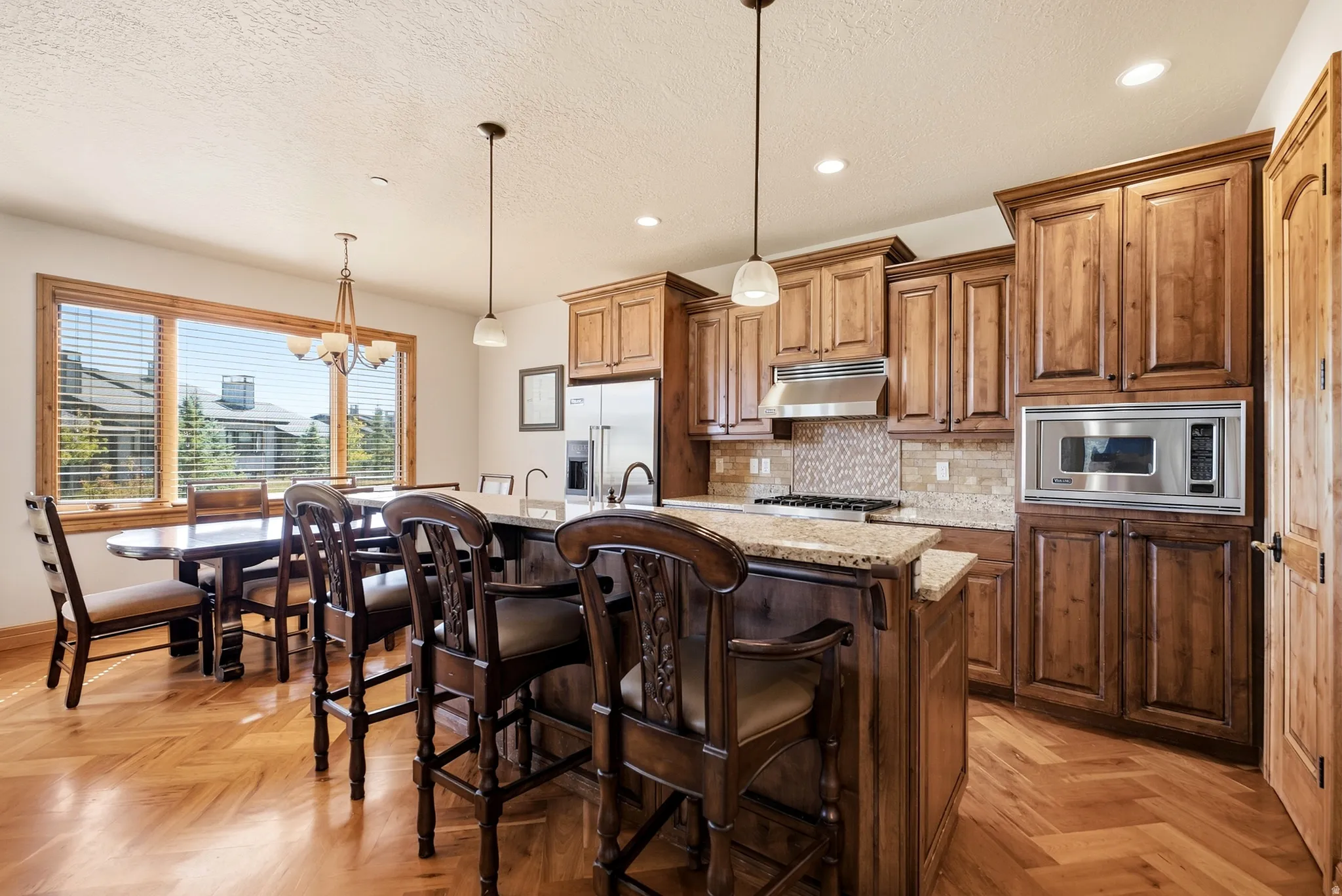 Kitchen featuring wood-finish flooring, granite countertops, wood cabinetry, a built-in stainless steel microwave, and pendant lighting
