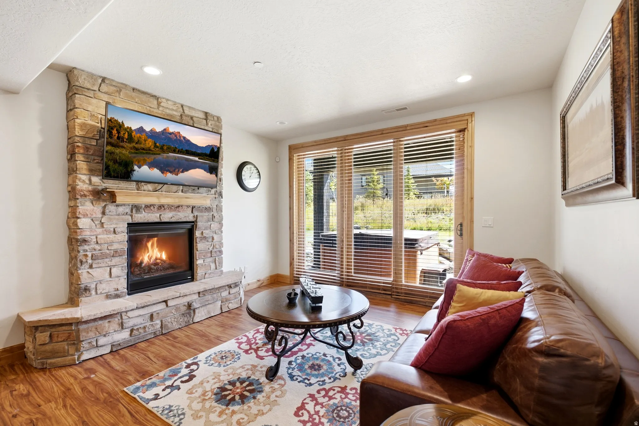 Stone-clad fireplace with hearth, wood-finish flooring, recessed lighting, and wooden-framed glass sliding doors