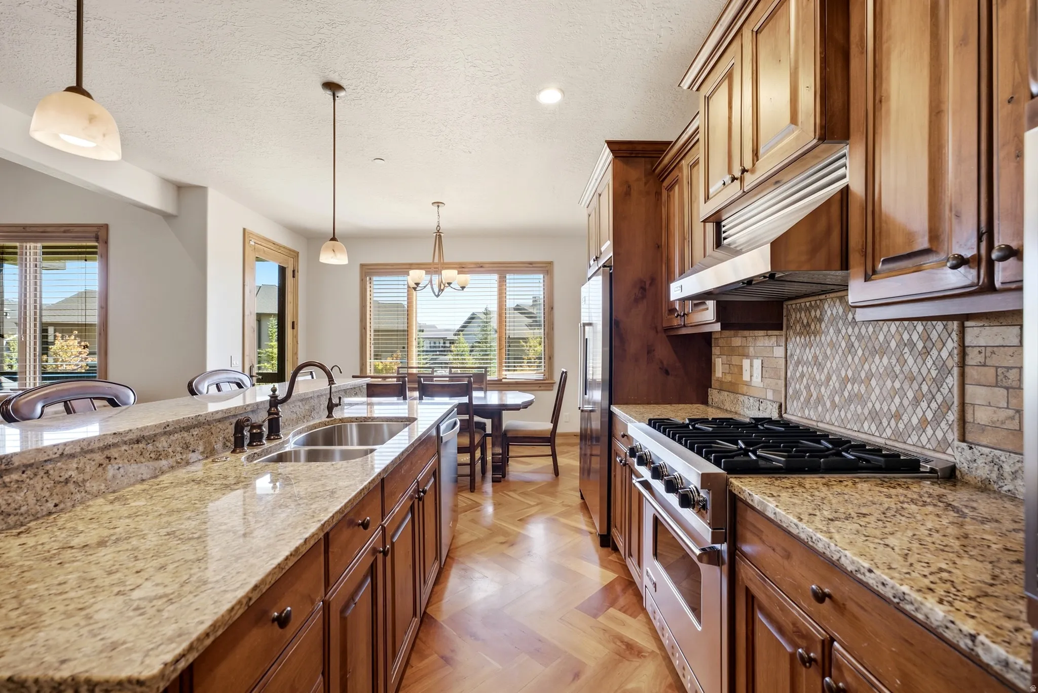 Gourmet kitchen with granite countertops, hardwood cabinetry, stainless steel appliances, and a herringbone wood-finish floor