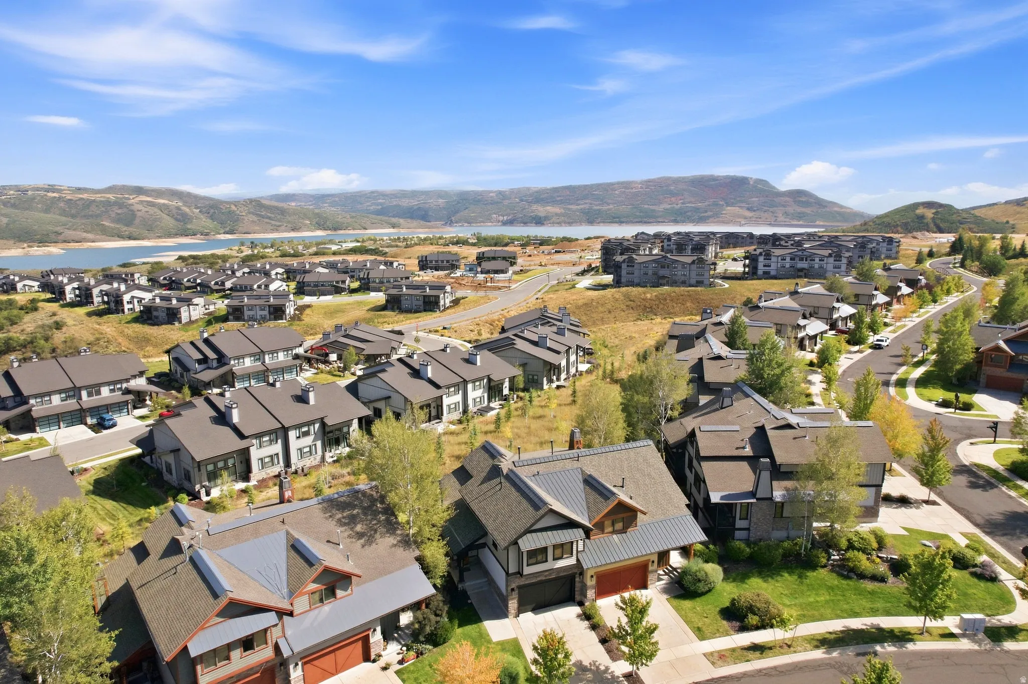Expansive community with modern residences, mature landscaping, and paved roadways, all set against a backdrop of distant hills and a large body of water