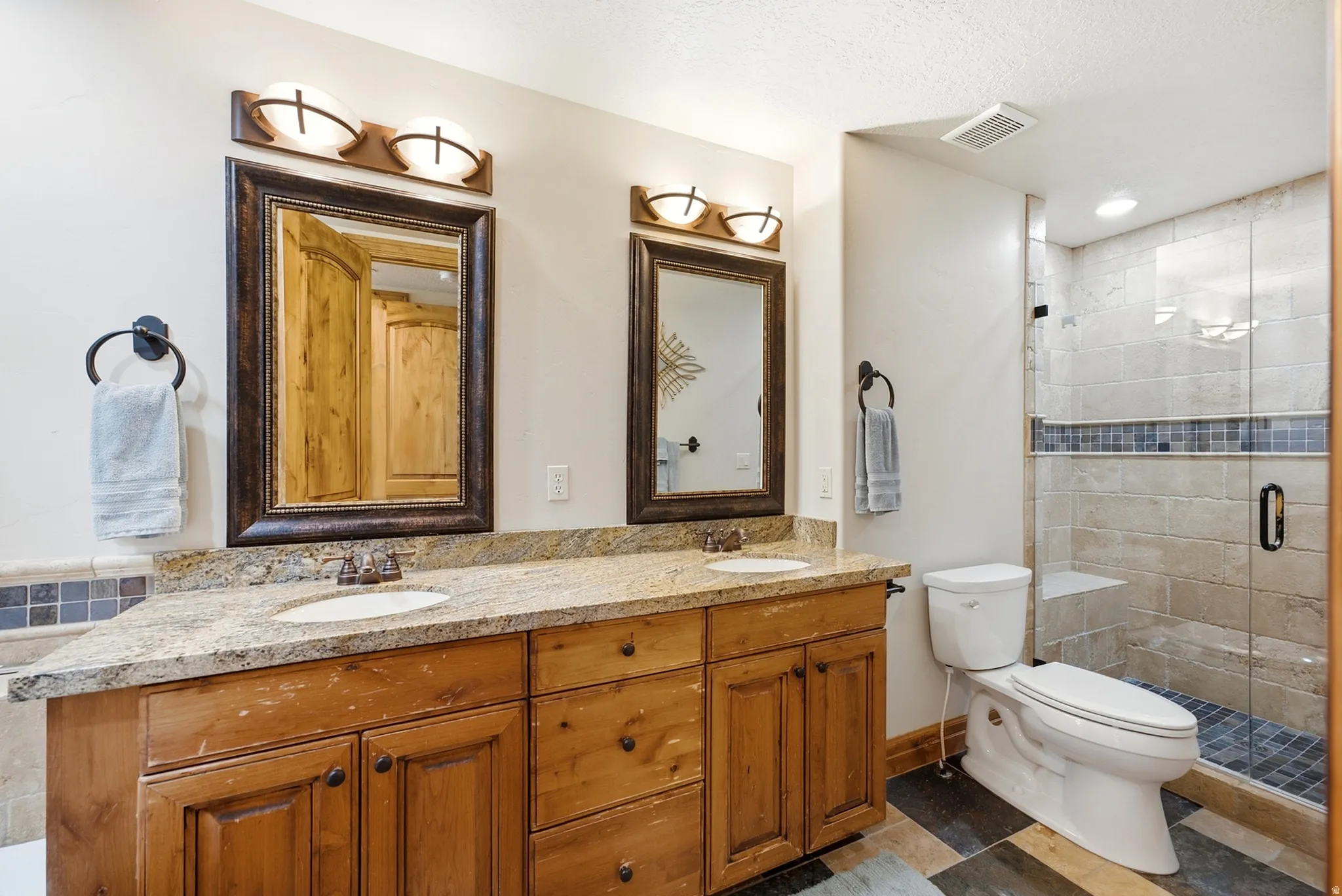 Dual vanity with granite countertop, wood-finish cabinetry, and individual framed mirrors