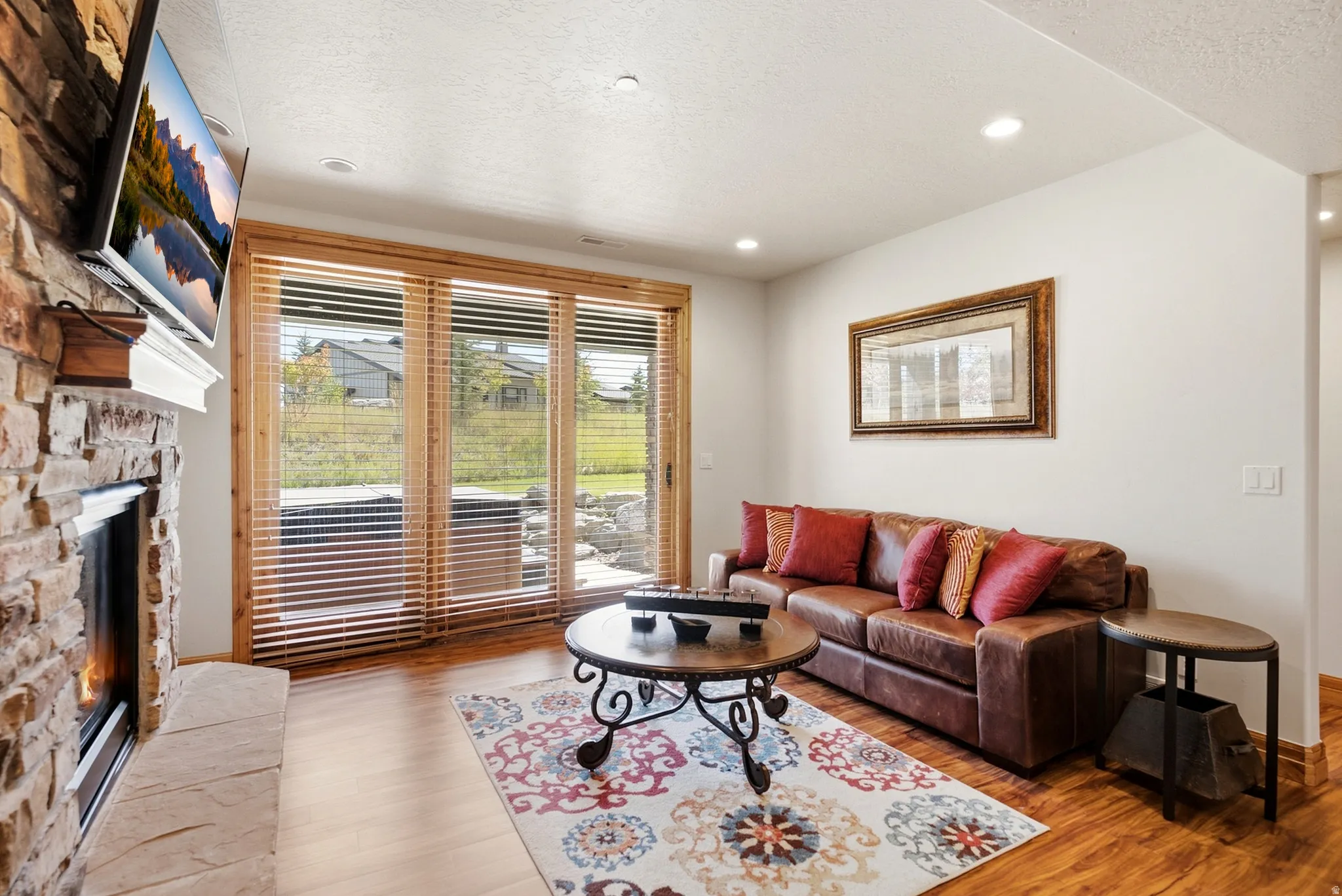 Stacked stone fireplace with mantel, hardwood-finish flooring, recessed lighting, and expansive glass sliding doors