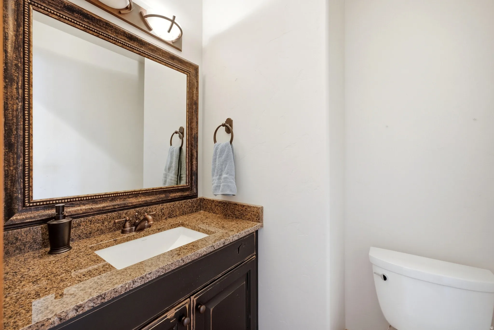 Vanity with a granite-style countertop, undermount sink, and dark wood-finish cabinetry