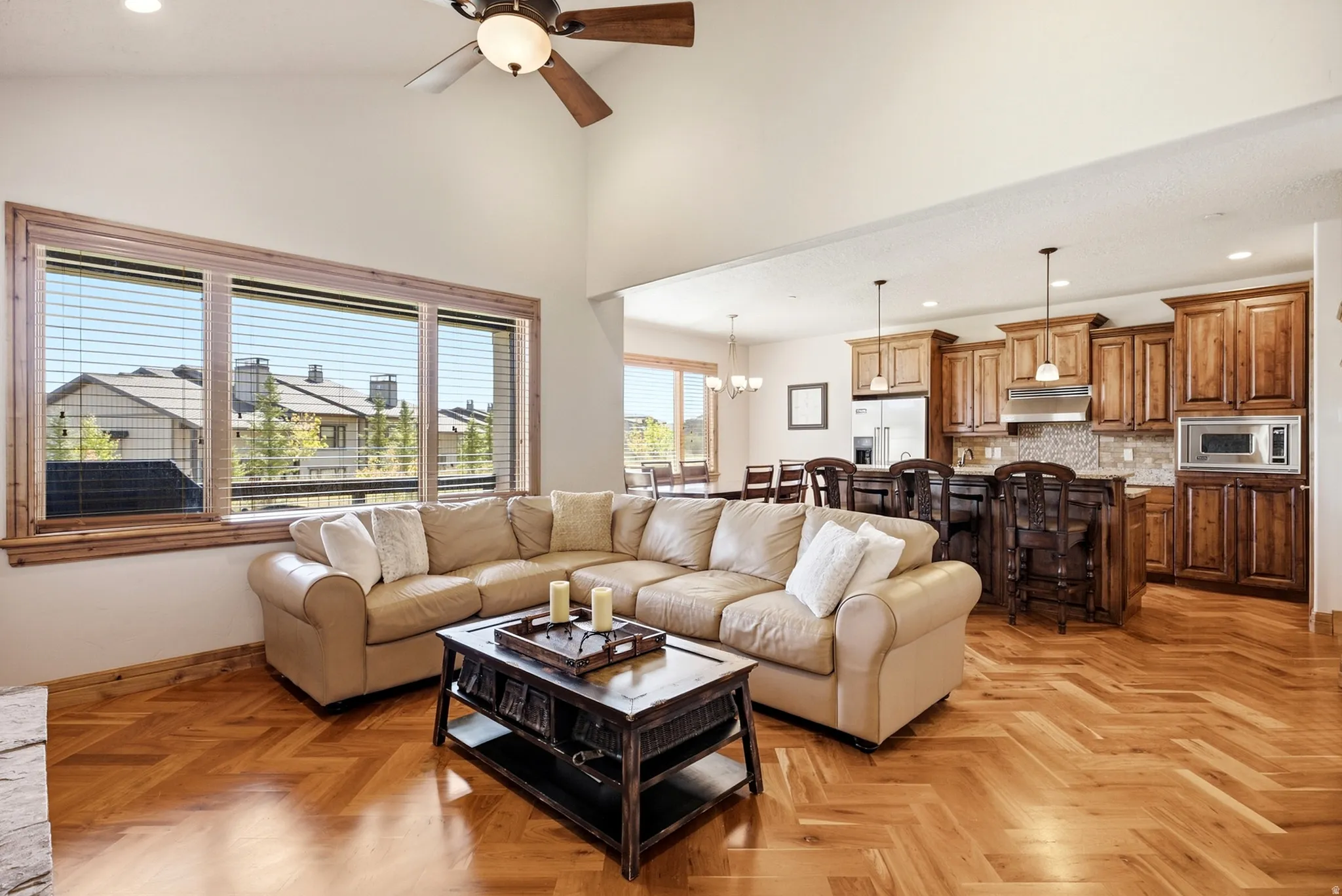 Vaulted ceiling, wood-finish flooring with herringbone pattern, ceiling fan, expansive windows with wood trim, and a kitchen with wood cabinetry