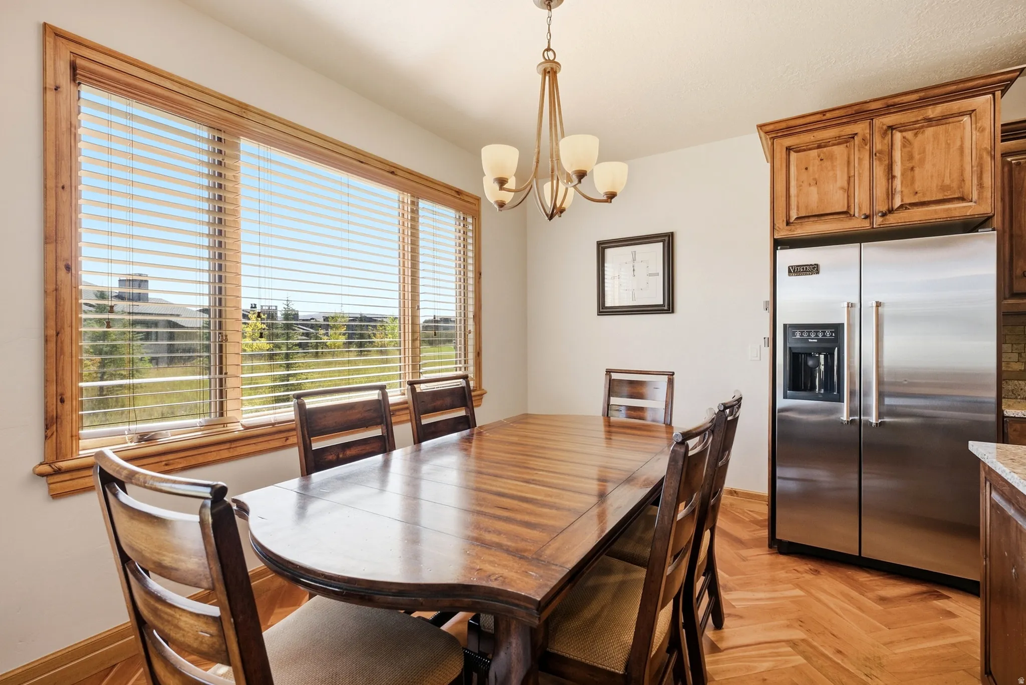 Spacious dining area featuring a large window with wood trim, wood-finish flooring, and a contemporary chandelier