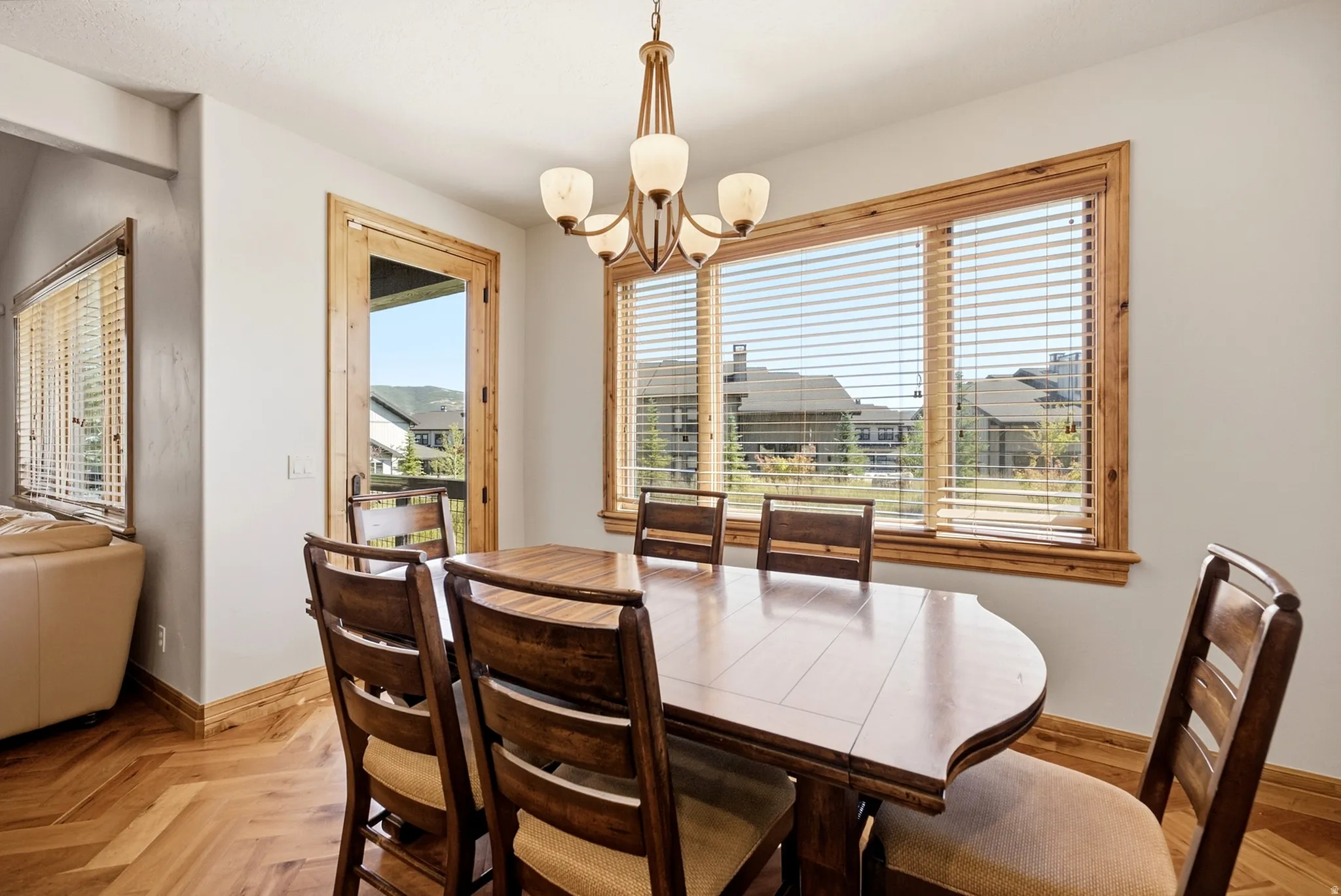 Herringbone wood-finish flooring, wood-trimmed windows with blinds, wood-trimmed glass door, and a bronze-finish chandelier