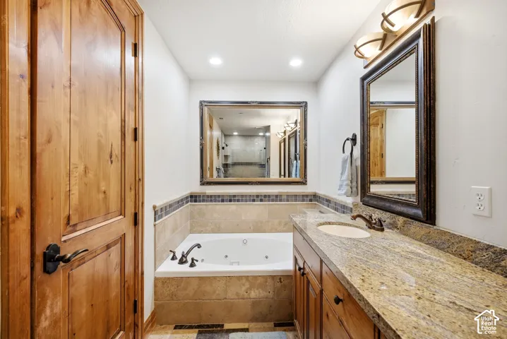 Built-in jetted tub surrounded by tile, granite-finish vanity with an undermount sink, and wood-finish cabinetry