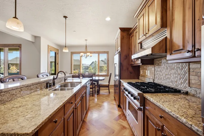 Gourmet kitchen with granite countertops, hardwood cabinetry, stainless steel appliances, and a herringbone wood-finish floor