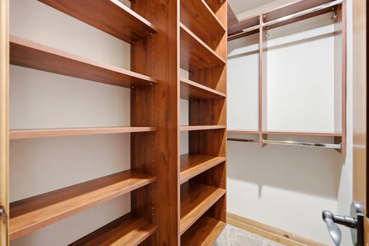 Built-in closet system featuring wood-finish shelving, hanging rods, and carpeted flooring