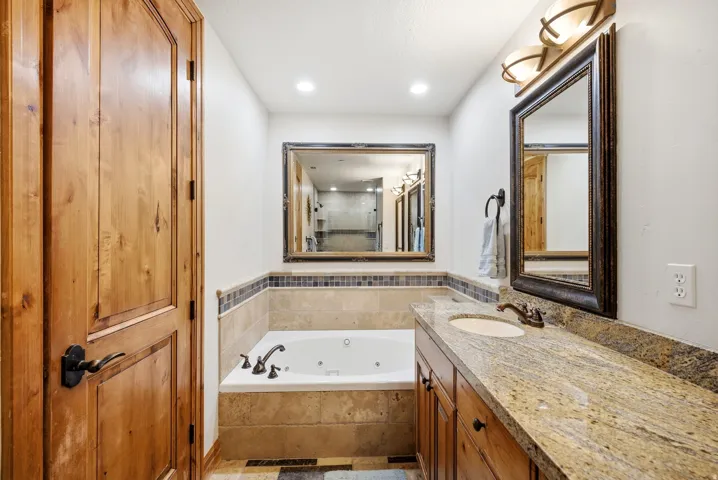 Built-in jetted tub surrounded by tile, granite-finish vanity with an undermount sink, and wood-finish cabinetry