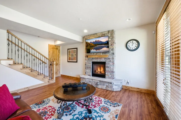 Stone-clad fireplace with a wood mantel, light wood-finish flooring, and a staircase featuring wrought iron balusters