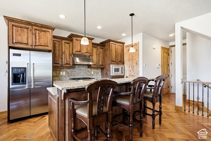 Kitchen featuring wood cabinetry, stainless steel appliances, a stone countertop island, and a decorative tile backsplash
