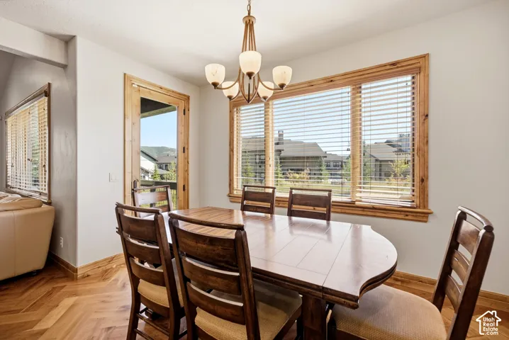 Herringbone wood-finish flooring, wood-trimmed windows with blinds, wood-trimmed glass door, and a bronze-finish chandelier