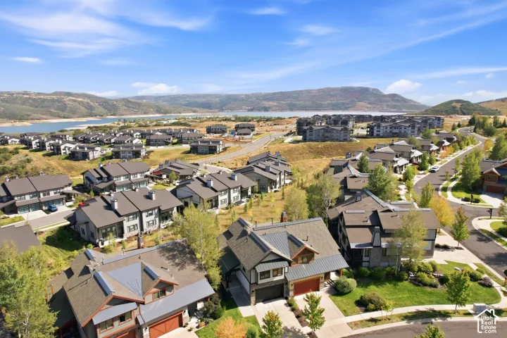 Expansive community with modern residences, mature landscaping, and paved roadways, all set against a backdrop of distant hills and a large body of water