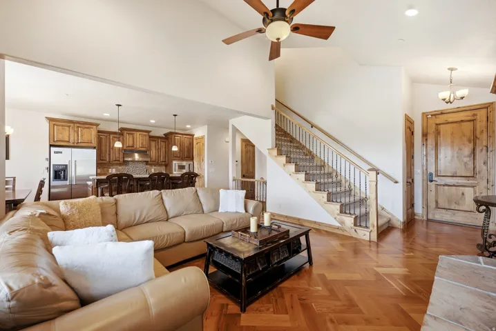 Herringbone wood-finish flooring, vaulted ceiling with wood-bladed ceiling fan, staircase with wrought iron balusters, natural wood interior doors, and stainless steel kitchen appliances
