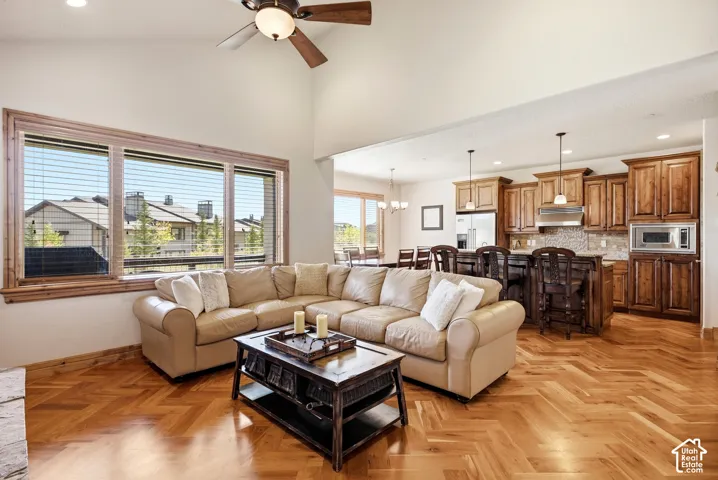 Vaulted ceiling, wood-finish flooring with herringbone pattern, ceiling fan, expansive windows with wood trim, and a kitchen with wood cabinetry
