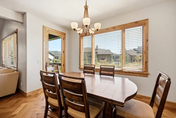 Herringbone wood-finish flooring, wood-trimmed windows with blinds, wood-trimmed glass door, and a bronze-finish chandelier